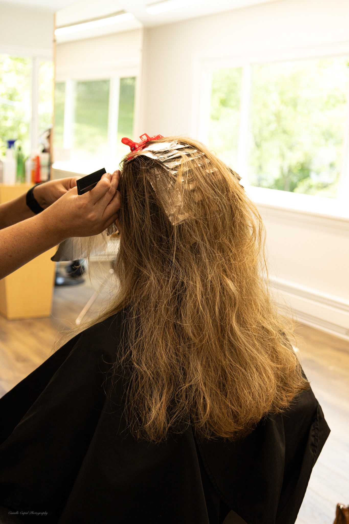 Hairdresser applying highlights to a client's hair with foil in a bright salon.