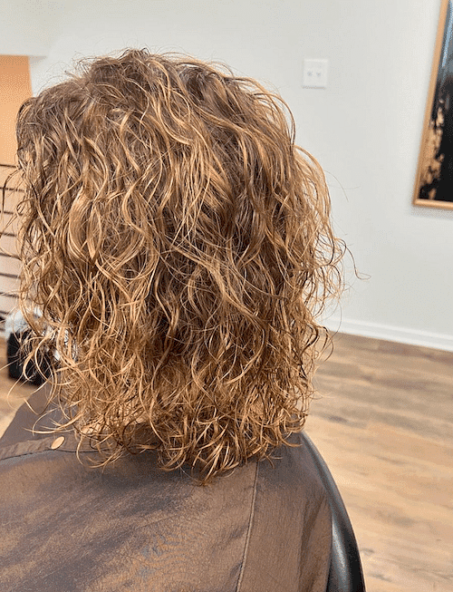 Person with curly, light brown hair sitting in a salon chair.