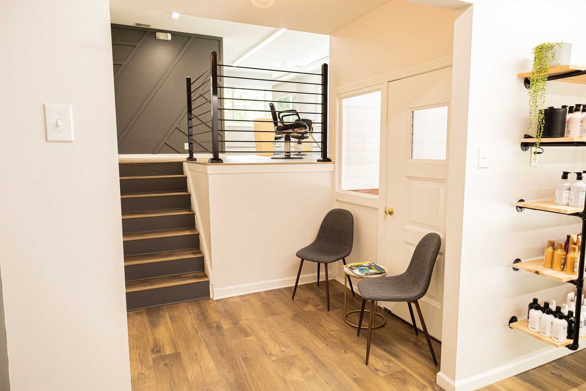 Modern waiting area with two chairs, a small table, and a staircase behind a railing.