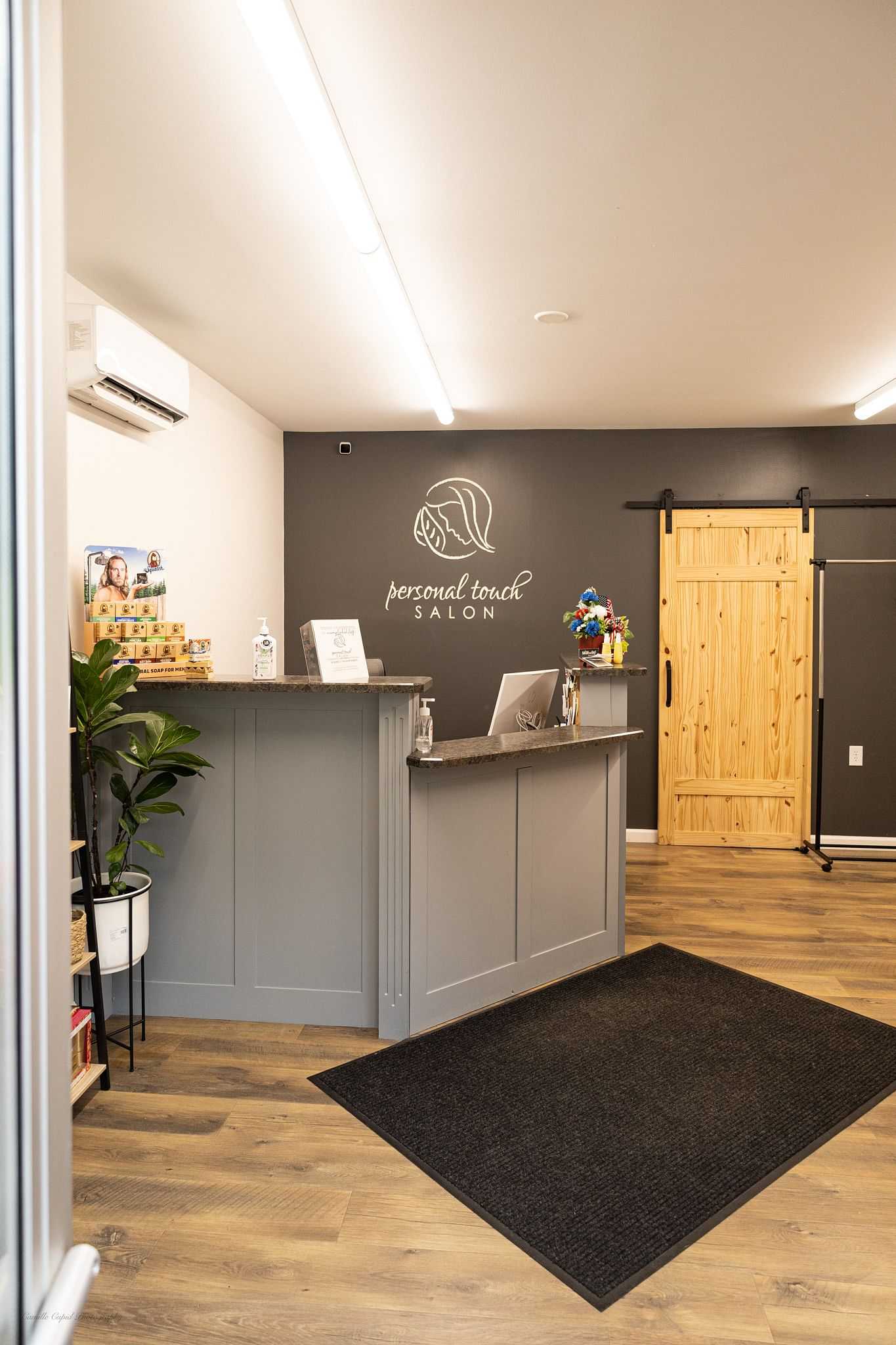 Modern salon reception with gray counter, wooden door, product shelf, and "personal touch salon" logo.